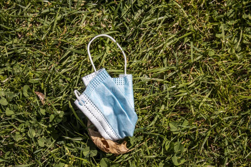Blå mask för medicinskt ansikte som faller samman på marken med döda blad på gräs och klöver. arkivfoto