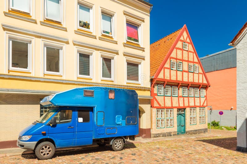 Blå motorhome parkerade nära en modern byggnad och ett gammalt hus i den traditionella tyska stilen royaltyfria bilder Blå motorhome parkerade nära en modern byggnad och ett gammalt hus i den traditionella tyska stilen royaltyfria bilder