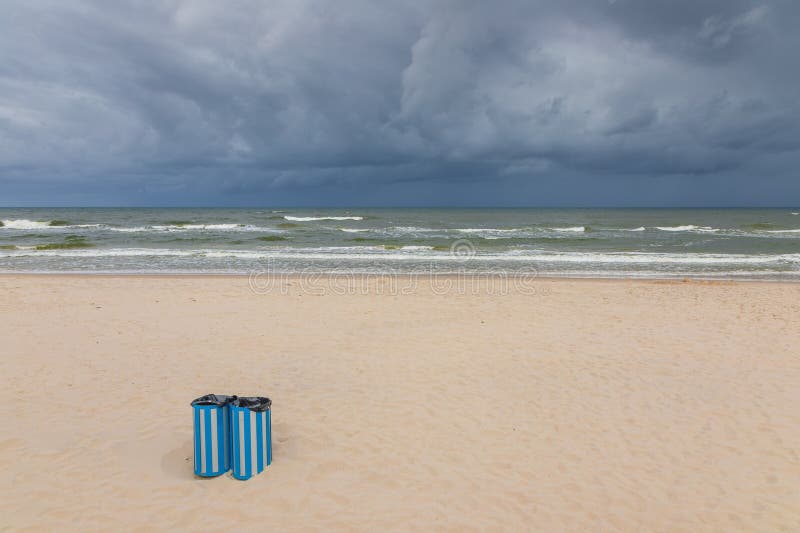 Blå soptunnor på den tomma stranden i Östersjön under stormiga himmel i Karwia Polen arkivfoto