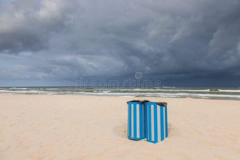 Blå soptunnor på den tomma stranden i Östersjön under stormiga himmel i Karwia Polen arkivfoton