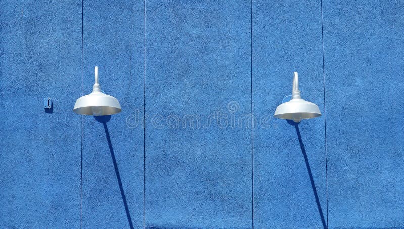 Blue stucco wall with light fixtures and shadows in daytime. Blue stucco wall with light fixtures and shadows in daytime