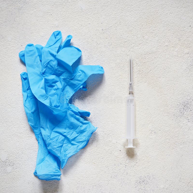 Blåa medicinska handskar och en medicinsk injektionsspruta på en ljus texturerad bakgrund Vaccineringobjekt, skott royaltyfri fotografi Blåa medicinska handskar och en medicinsk injektionsspruta på en ljus texturerad bakgrund Vaccineringobjekt, skott royaltyfri fotografi