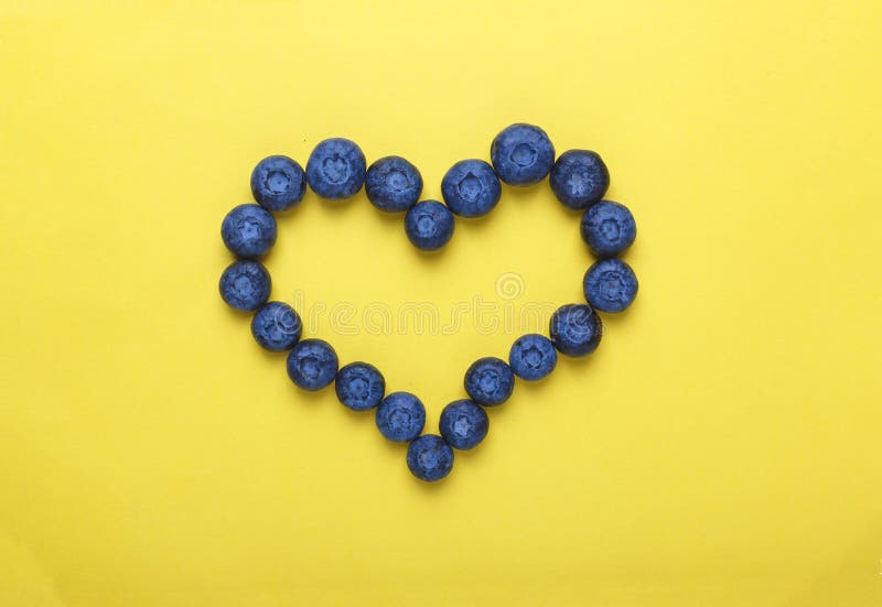 Blåbär i formen av hjärta på en gul bakgrund Begreppet: blåbär förhindrar hjärtsjukdomstilminimalism