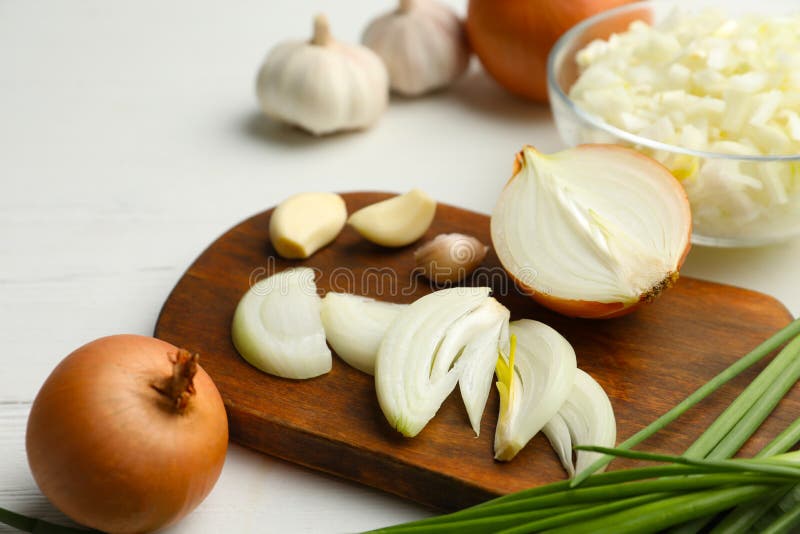 Board with cut onion and garlic on white table