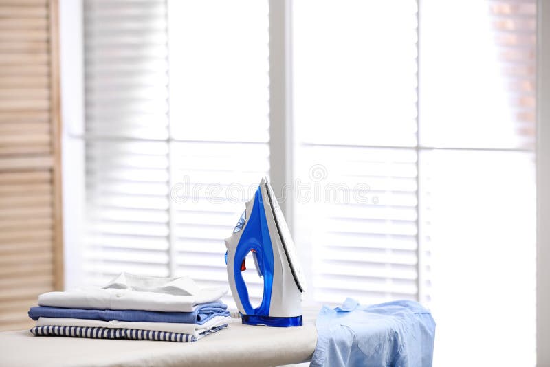 Board with modern iron and stack of clothes indoors. Laundry day royalty free stock photos