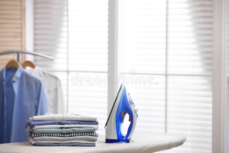 Board with modern iron and stack of clothes, space for text. Laundry day royalty free stock photo