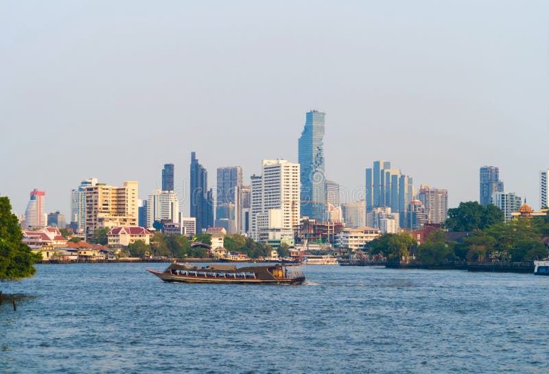 Boats cruise at Chao Phraya River with skyscraper buildings in Bangkok Downtown, urban city with blue sky, Thailand. Architecture