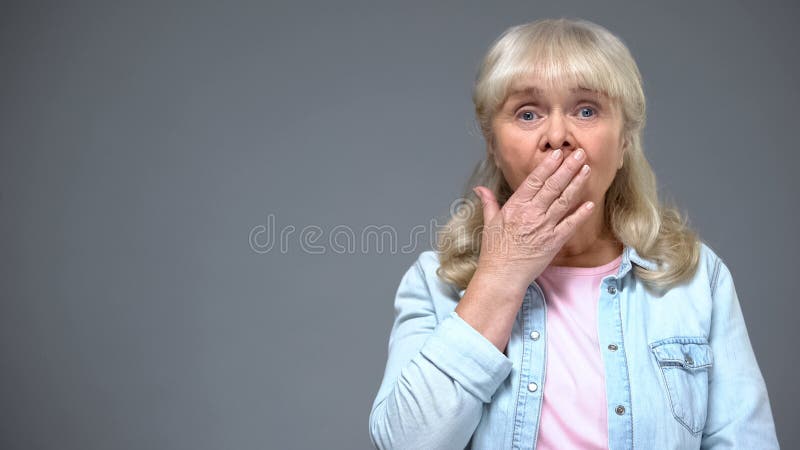 Boca de envejecimiento chocada de la cubierta de la mujer con la mano, asombrosa con noticias, emociones fotografía de archivo