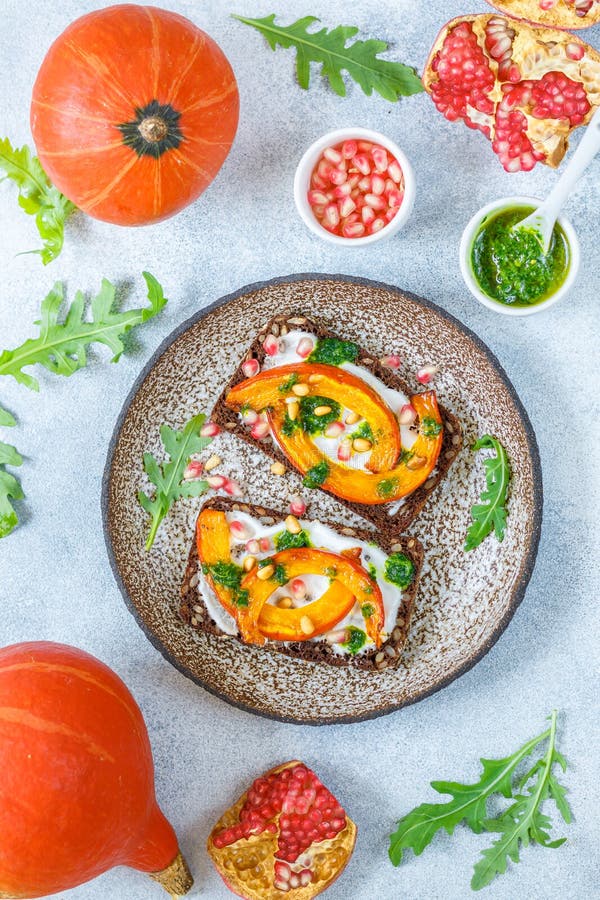 Bocadillos del pan de Rye con la calabaza, el pesto, el arugula, semillas de la granada y nueces de pino cocidos imagen de archivo libre de regalías Bocadillos del pan de Rye con la calabaza, el pesto, el arugula, semillas de la granada y nueces de pino cocidos imagen de archivo libre de regalías