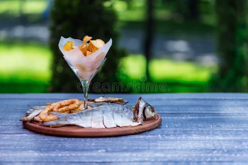 Bocados para la cerveza Patatas saladas, secadas de los pescados, del anillo del calamar y fritas, en la tabla de cortar y el fon fotografía de archivo Bocados para la cerveza Patatas saladas, secadas de los pescados, del anillo del calamar y fritas, en la tabla de cortar y el fon fotografía de archivo