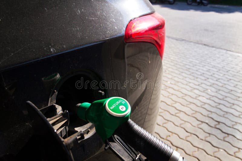 Fuel nozzle with new EU labeling circle gasoline type E5 filling car tank from petrol station dispenser, black car. Fuel nozzle with new EU labeling circle gasoline type E5 filling car tank from petrol station dispenser, black car