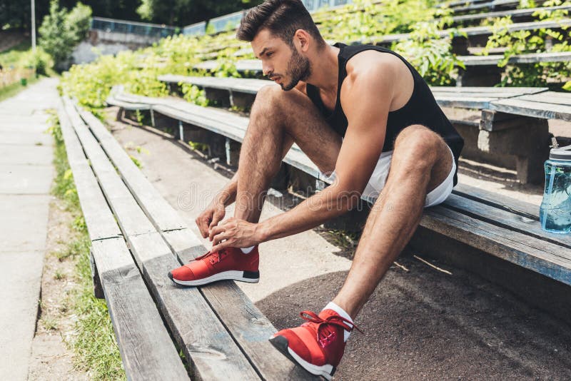boczny widok wiąże shoelaces sportowiec podczas gdy siedzący na ławce przy sportem obrazy royalty free boczny widok wiąże shoelaces sportowiec podczas gdy siedzący na ławce przy sportem obrazy royalty free