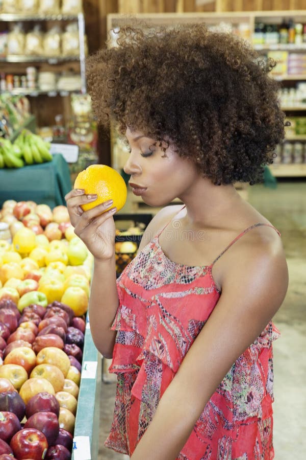 Side view of African American women smelling fresh orange at supermarket. Side view of African American women smelling fresh orange at supermarket