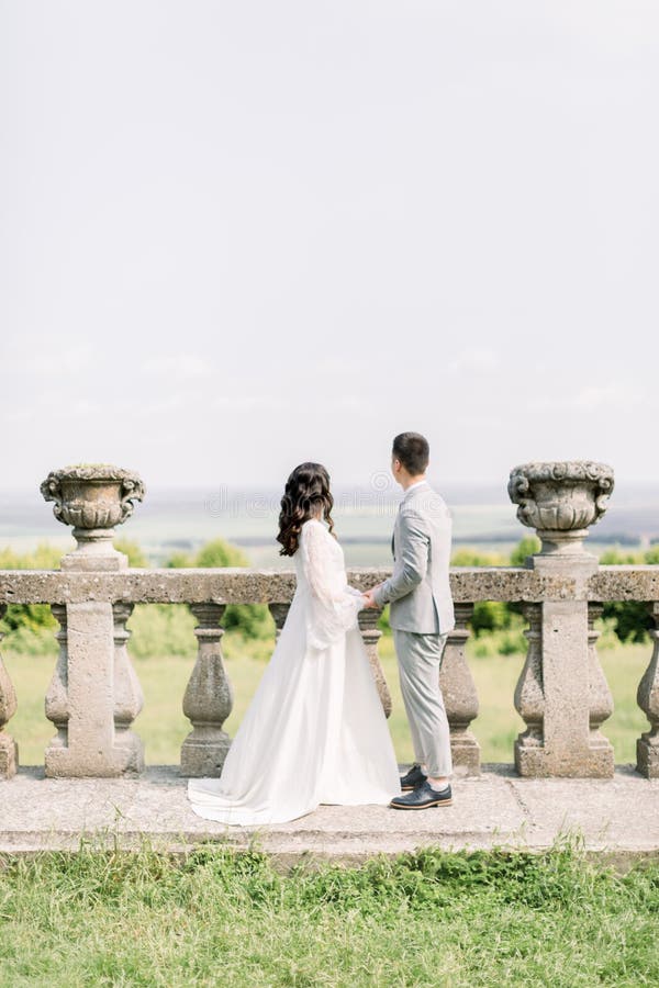Boda de la hermosa pareja china en el soleado dÃa en el antiguo castillo, posando y tomando las manos cerca de las antiguas baran fotografía de archivo libre de regalías Boda de la hermosa pareja china en el soleado dÃa en el antiguo castillo, posando y tomando las manos cerca de las antiguas baran fotografía de archivo libre de regalías
