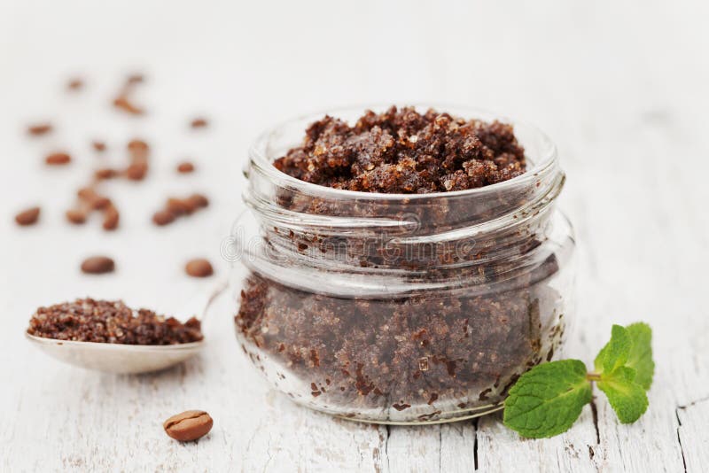 Body scrub of ground coffee, sugar and coconut oil in glass jar on white rustic table, homemade cosmetic for peeling and spa care