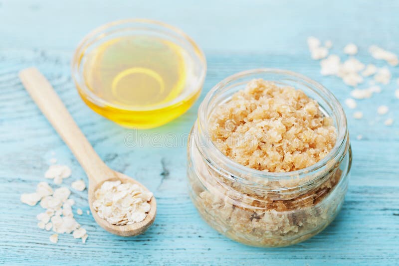 Body scrub of oatmeal, sugar, honey and oil in glass jar on blue rustic table, homemade cosmetic for peeling and spa care
