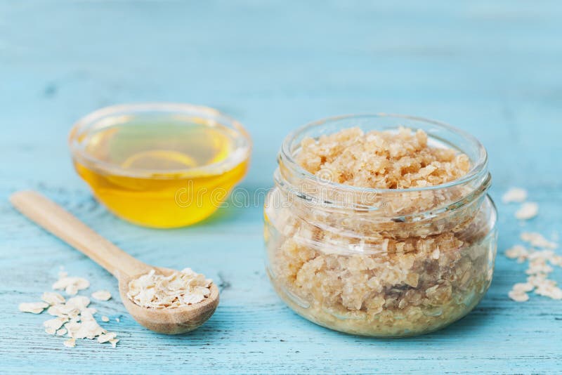 Body scrub of oatmeal, sugar, honey and oil in glass jar on blue rustic table, homemade cosmetic for peeling and spa care