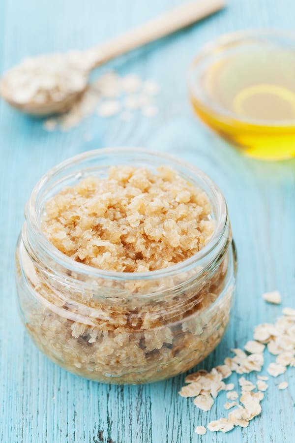 Body scrub of oatmeal, sugar, honey and oil in glass jar on blue rustic table, homemade cosmetic for peeling and spa care