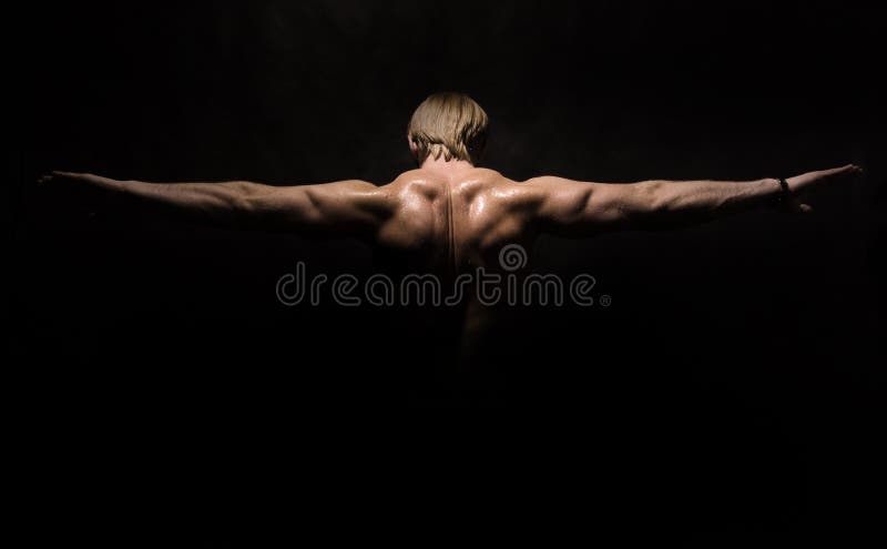 Bodybuilder showing his back and arms muscles, on black studio background.