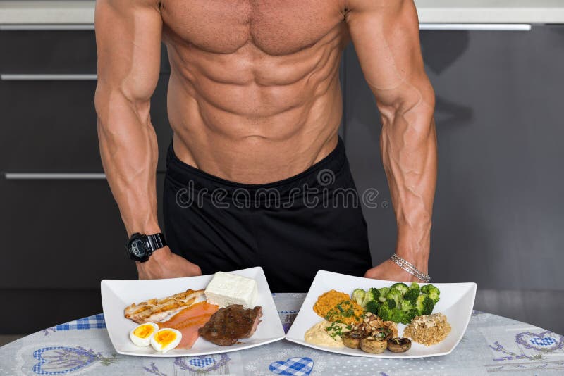Fit young man. bodybuilder in the kitchen; animal versus plant proteins: plate with beef, eggs, salmon, cheese and chicken grill and another with nuts, mushrooms, broccoli, lentil, hummus and quinoa