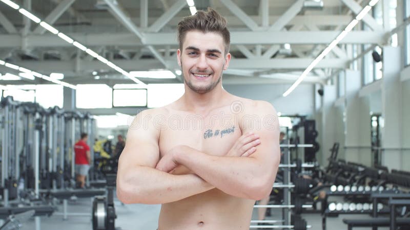 Bodybuilder masculin blond sans chemise attirant en bref à l'intérieur dans le gymnase foncé, montrant le torse musculaire et l'A