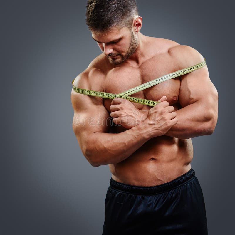 Closeup of bodybuilder holding tape measure. Cropped image of muscular arm  holding measuring tape isolated over gray background. Wrong muscle measuring.  Photos