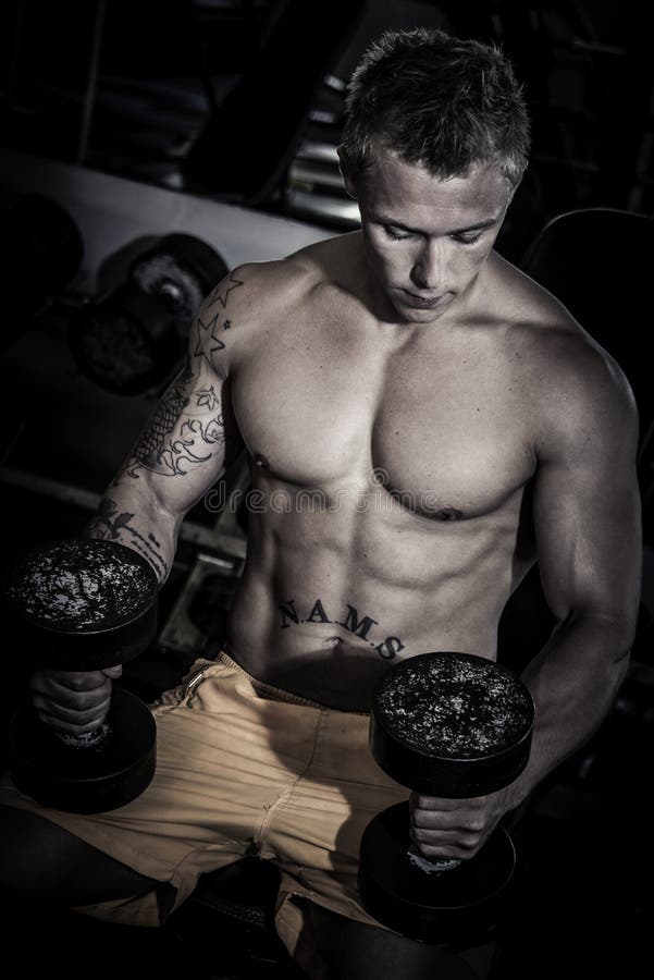 Bodybuilder standing with a dumbbell after training in the gym. Bodybuilder standing with a dumbbell after training in the gym