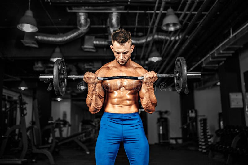 Young handsome caucasian bodybuilder sportsman working out with a barbell in gym, doing biceps training.