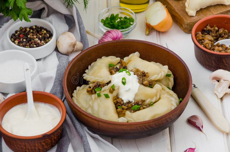 Boiled dumplings vareniki with potatoes and fried mushrooms with onions in a bowl with sour cream and green onions.