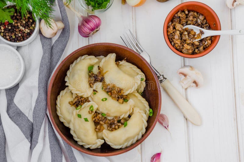 Boiled Vegan dumplings vareniki with potatoes and fried mushrooms with onions in a bowl on a white wooden background.