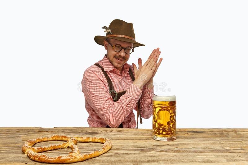 Portrait of delightful bearded man in hat and traditional Bavarian costume with glass of frothy beer and fresh with golden brown pretzel. Concept of Oktoberfest, traditions, drinks and food. Ad. Portrait of delightful bearded man in hat and traditional Bavarian costume with glass of frothy beer and fresh with golden brown pretzel. Concept of Oktoberfest, traditions, drinks and food. Ad