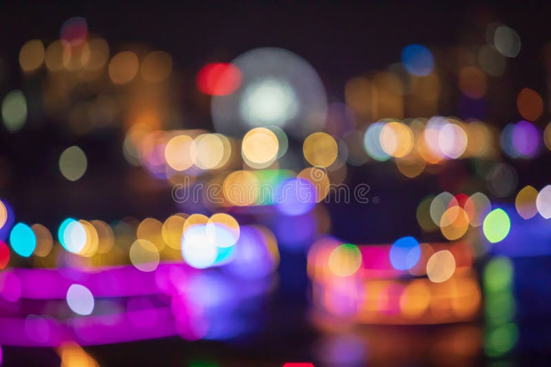 Bokeh abstract blur from street or road and ferris wheel lights and car or boat in river or lake at night of the city or town.