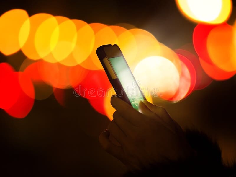 Bokeh colorido de la luz de la noche de la pantalla del teléfono elegante de la mano de la mujer que brilla intensamente imagen de archivo Bokeh colorido de la luz de la noche de la pantalla del teléfono elegante de la mano de la mujer que brilla intensamente imagen de archivo