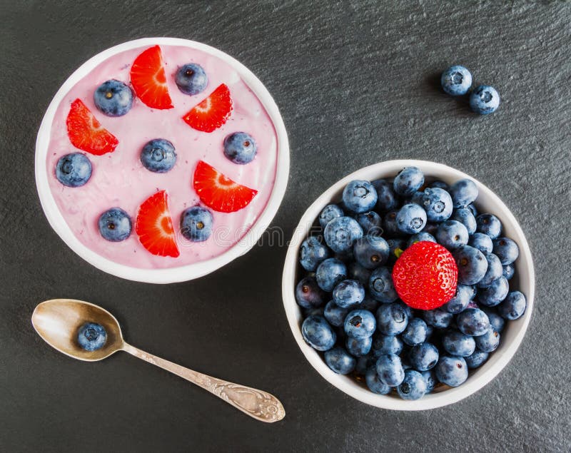 Bol de petit déjeuner avec du yaourt, le muesli, les myrtilles fraîches et les fraises Fond en pierre noir, vue supérieure photo stock Bol de petit déjeuner avec du yaourt, le muesli, les myrtilles fraîches et les fraises Fond en pierre noir, vue supérieure photo stock