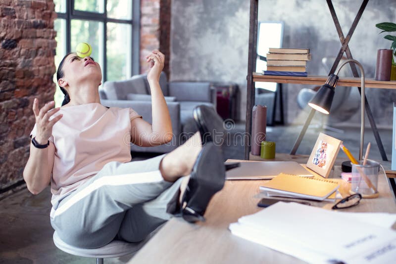 Break from work. Pleasant female employee putting legs on table and playing with ball. Break from work. Pleasant female employee putting legs on table and playing with ball