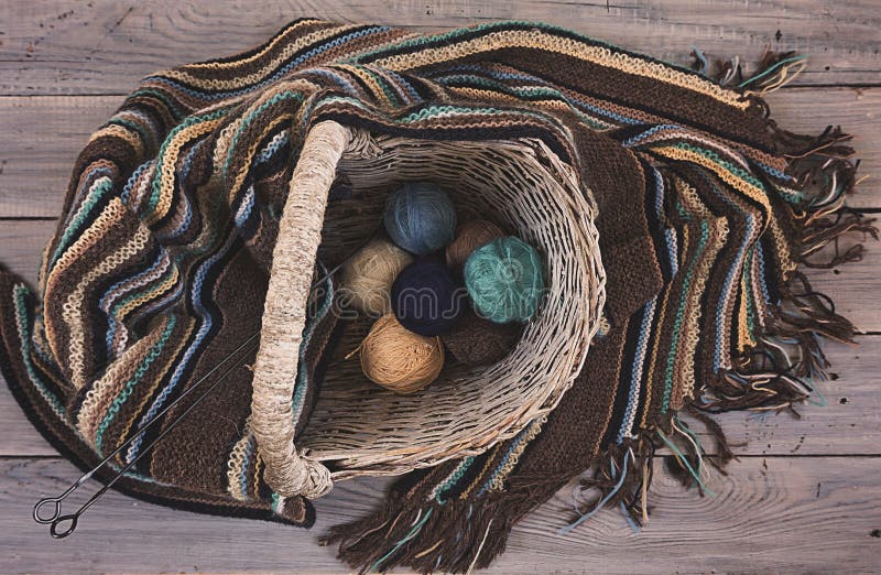 Bolas de lana hechas punto de la bufanda y del hilado en una cesta de mimbre en una madera foto de archivo Bolas de lana hechas punto de la bufanda y del hilado en una cesta de mimbre en una madera foto de archivo
