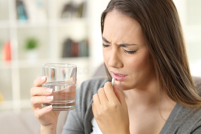 Painful woman taking a pill sitting on a sofa in the living room in a house interior. Painful woman taking a pill sitting on a sofa in the living room in a house interior