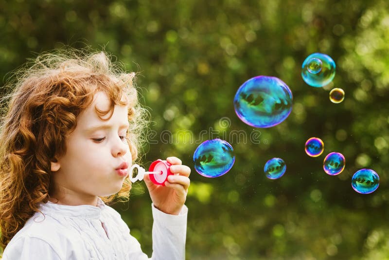 Little girl blowing soap bubbles, closeup portrait beautiful curly baby. Little girl blowing soap bubbles, closeup portrait beautiful curly baby