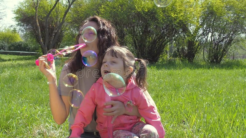 Bolhas de sabão do sopro da mamã e da filha Família no ar livre Família feliz no parque que joga com bolhas