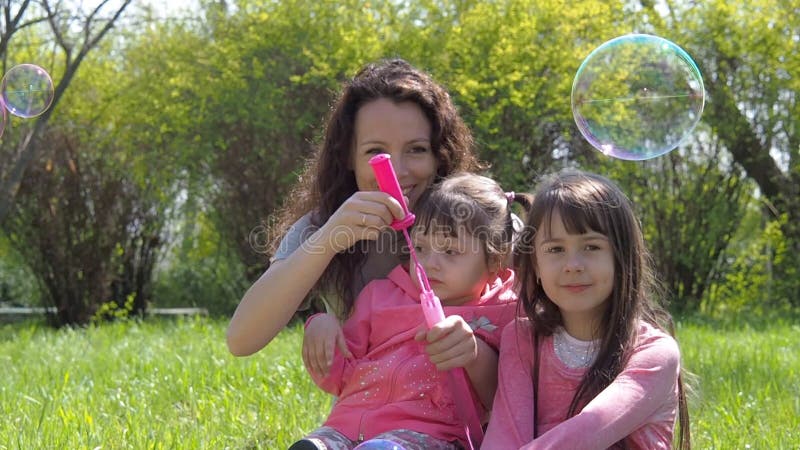 Bolhas do sopro da mamã e da filha Família no parque As crianças com mamã estão jogando com bolhas Família feliz na natureza