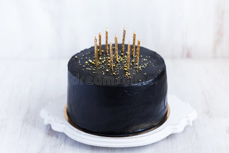 Mãos acendem velas no bolo o bolo de férias é decorado com bolas douradas,  brilhos dourados e macaroons pretos bolo de aniversário masculino 60 anos  fechar