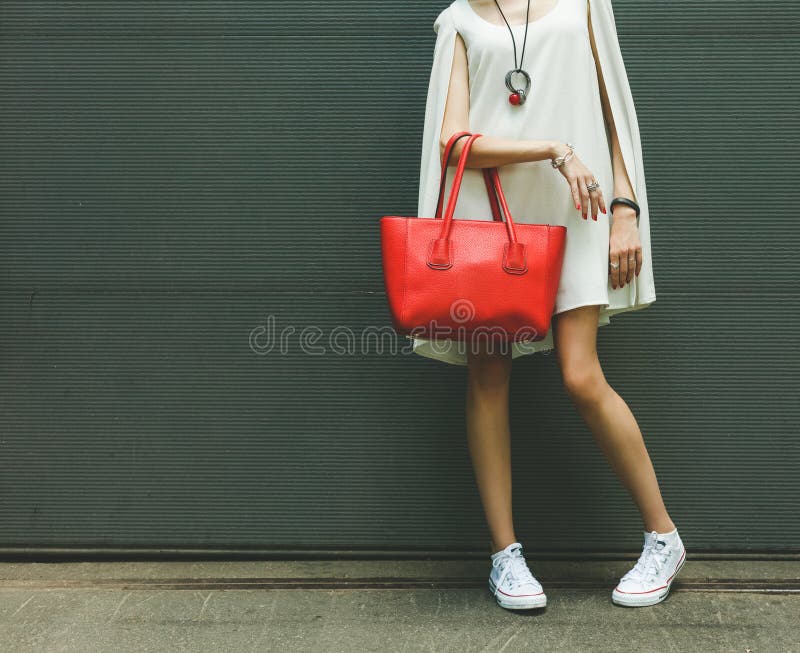 Bolsa vermelha grande bonita elegante no braço da menina em um vestido branco elegante, levantando perto da parede na foto de stock Bolsa vermelha grande bonita elegante no braço da menina em um vestido branco elegante, levantando perto da parede na foto de stock