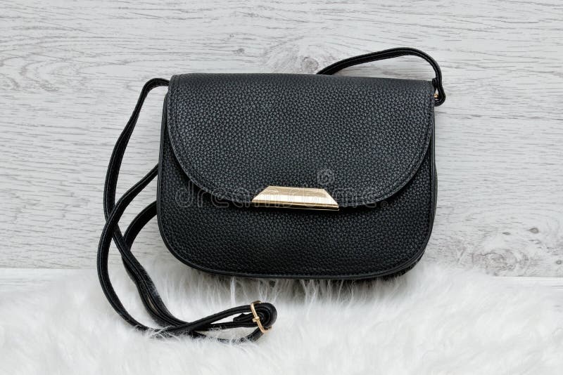 Bolso negro en una piel blanca, fondo de madera ligero fotografía de archivo Bolso negro en una piel blanca, fondo de madera ligero fotografía de archivo