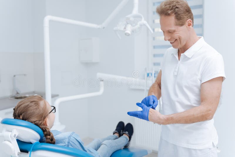 Bom dentista qualificado que põe sobre luvas especiais foto de stock Bom dentista qualificado que põe sobre luvas especiais foto de stock