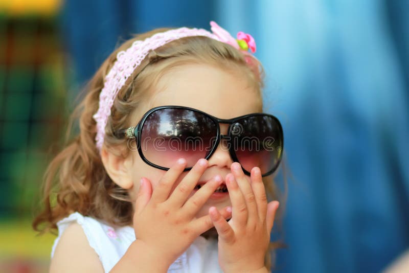 Bonbon une fille an qui lunettes de soleil du ` s de maman volées par s de ` et heureux de les porter essayant de ressembler à l' photographie stock libre de droits Bonbon une fille an qui lunettes de soleil du ` s de maman volées par s de ` et heureux de les porter essayant de ressembler à l' photographie stock libre de droits