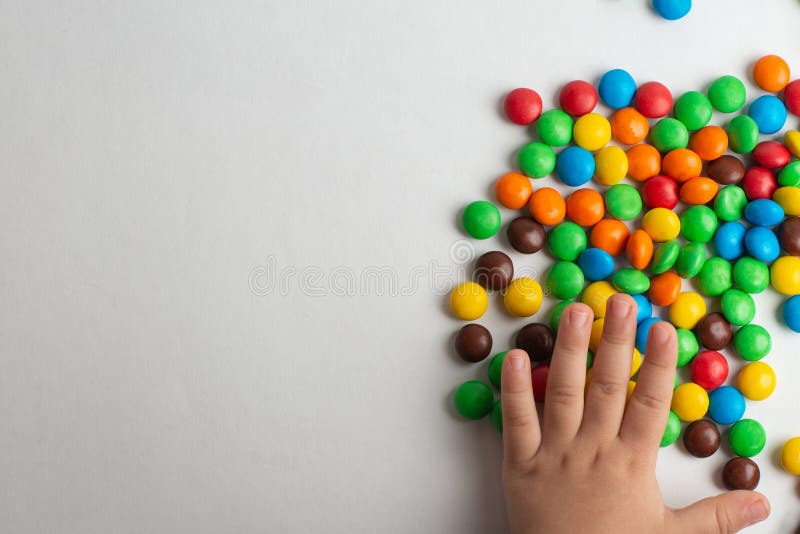 Bonbons au chocolat colorés sur le fond blanc avec la main d'enfant images stock Bonbons au chocolat colorés sur le fond blanc avec la main d'enfant images stock
