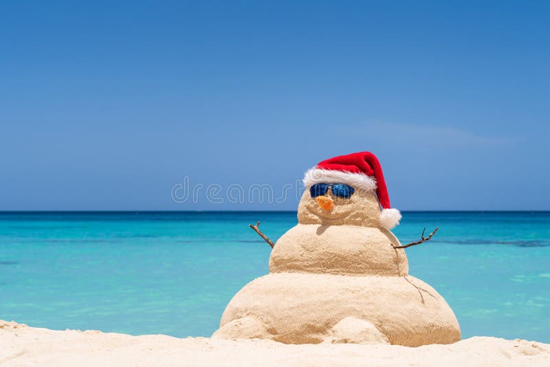 Bonhomme de neige arénacé de sourire avec le chapeau rouge de Santa sur la plage des Caraïbes Concept de vacances pour la nouvell image stock Bonhomme de neige arénacé de sourire avec le chapeau rouge de Santa sur la plage des Caraïbes Concept de vacances pour la nouvell image stock