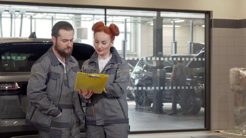Bonita mecânica de carros femininos discutindo trabalho com colega macho na garagem foto de stock Bonita mecânica de carros femininos discutindo trabalho com colega macho na garagem foto de stock