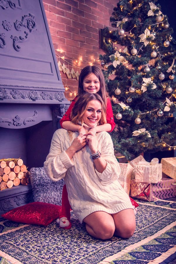 Bonita niña y su hermosa joven madre cerca de la chimenea con leña y árbol de Navidad Año Nuevo, 2020, Navidad foto de archivo libre de regalías