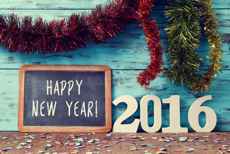 Tinsel of different colors and a chalkboard with the text happy new year written in it and three-dimensional white numbers forming the number 2016, on a rustic wooden surface sprinkled with confetti. Tinsel of different colors and a chalkboard with the text happy new year written in it and three-dimensional white numbers forming the number 2016, on a rustic wooden surface sprinkled with confetti